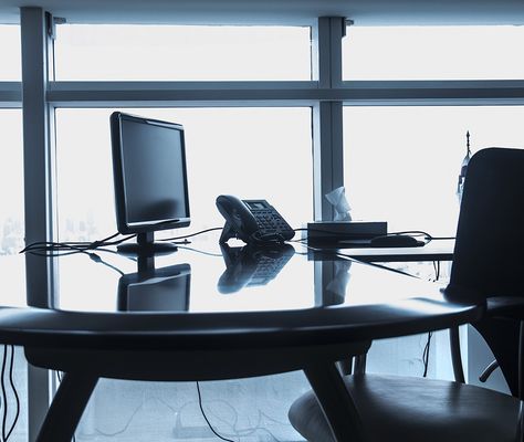 A desk with a monitor and a desk phone in front of a floor-to-ceiling window